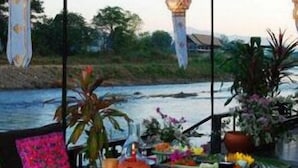 Uma área de refeições ao ar livre com uma mesa posta para dois, com vista para um rio.