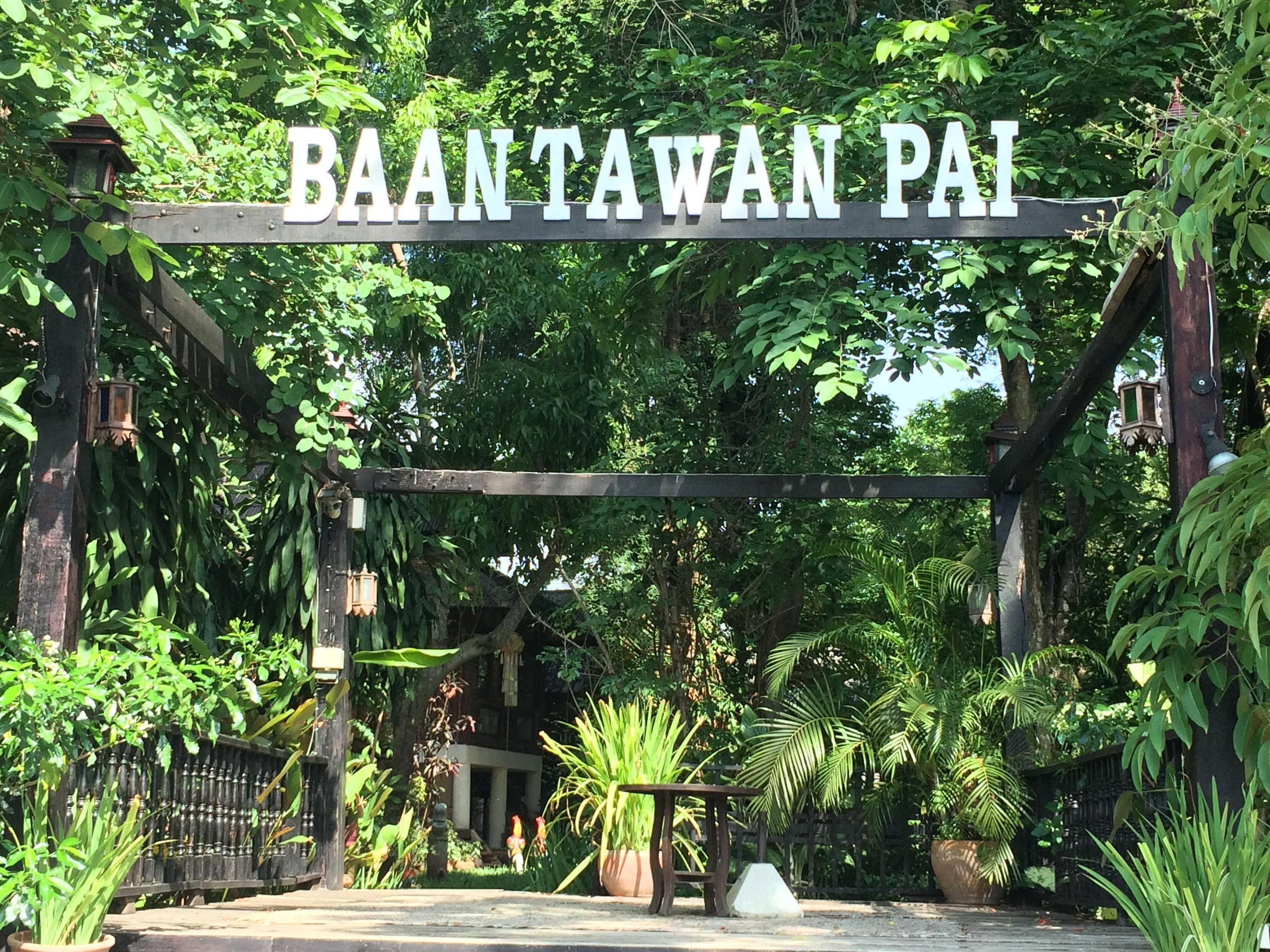 Ein Schild mit der Aufschrift "BAANTAWAN PAI" über einem Tor, umgeben von üppiger Vegetation und einem traditionellen Laternenpfahl.