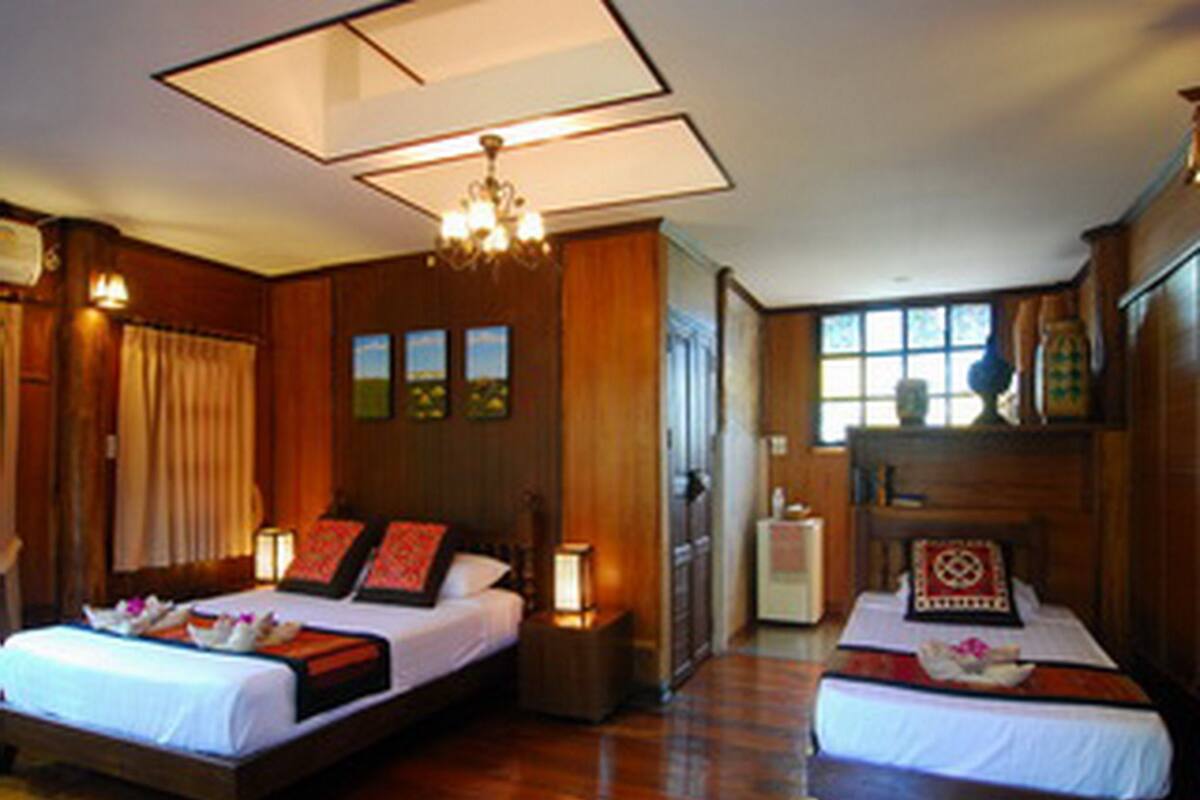 A hotel room with two beds, wooden flooring, a chandelier, and a view of the outdoors through the window.