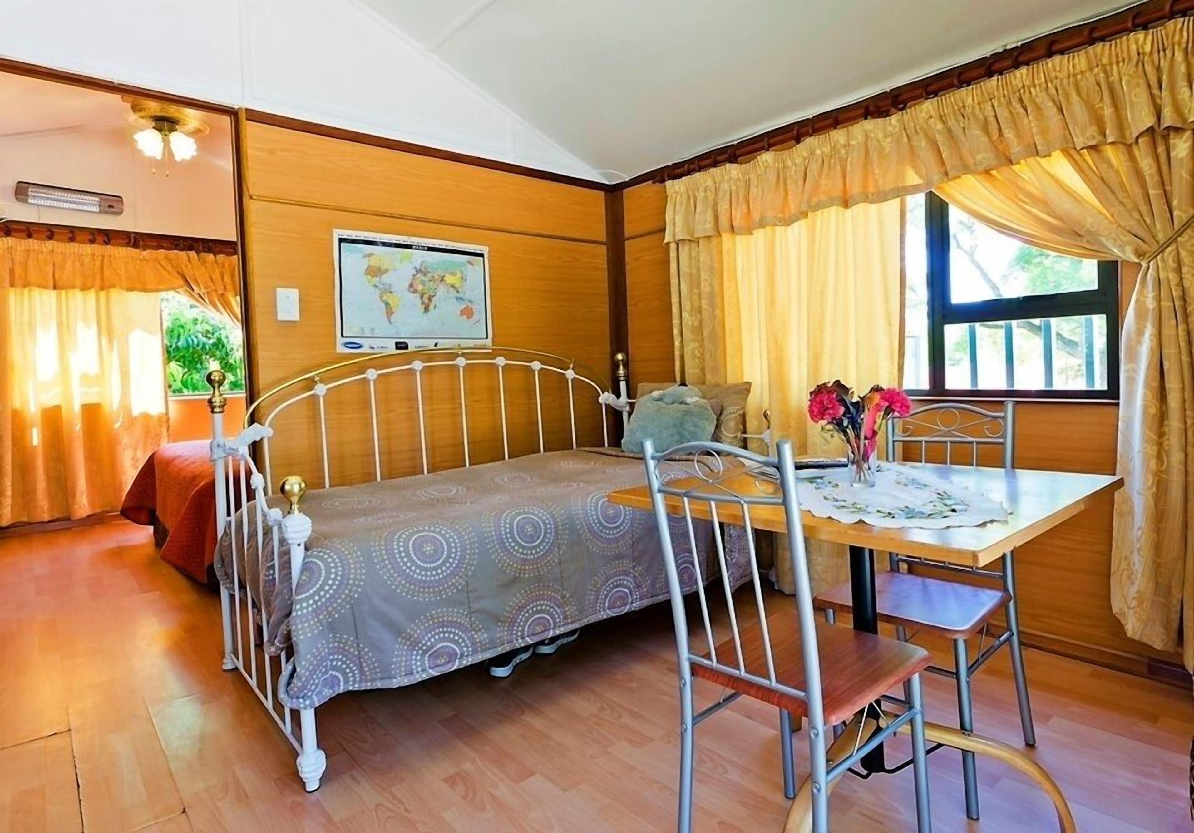 A room with a bed, a table with chairs, a map on the wall, and curtains.