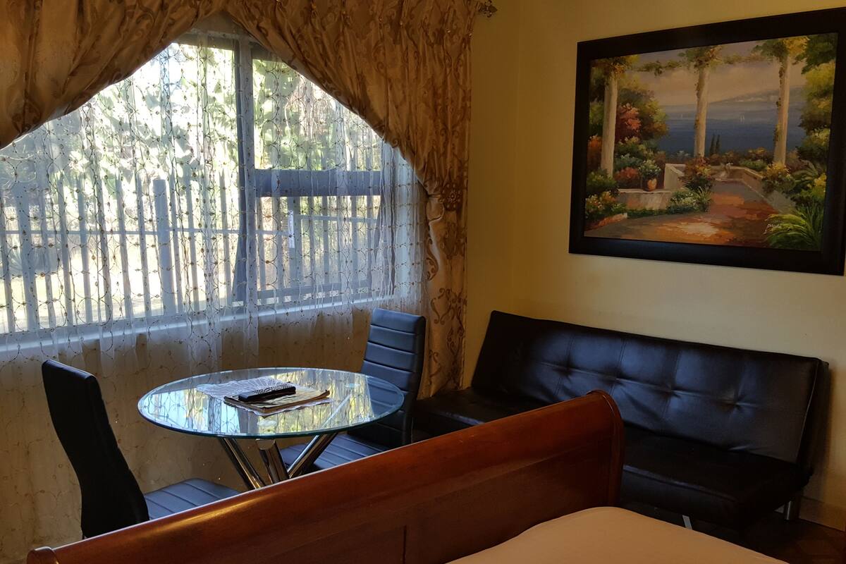 Una habitación con una cama, una mesa redonda de cristal, un sofá de cuero negro y un cuadro en la pared.