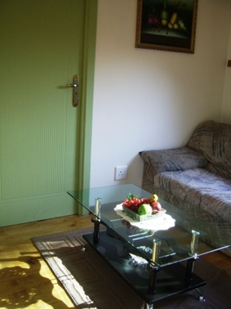 A room with a glass-top table, a green door, a couch, and a painting on the wall.