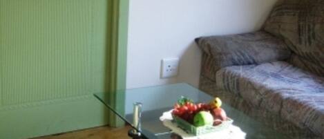 A room with a glass-top table, a green door, a couch, and a painting on the wall.