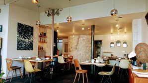 A modern restaurant with multiple dining tables and chairs, a map on the wall, and pendant lighting. - Accostage Hotel (La Rochelle)