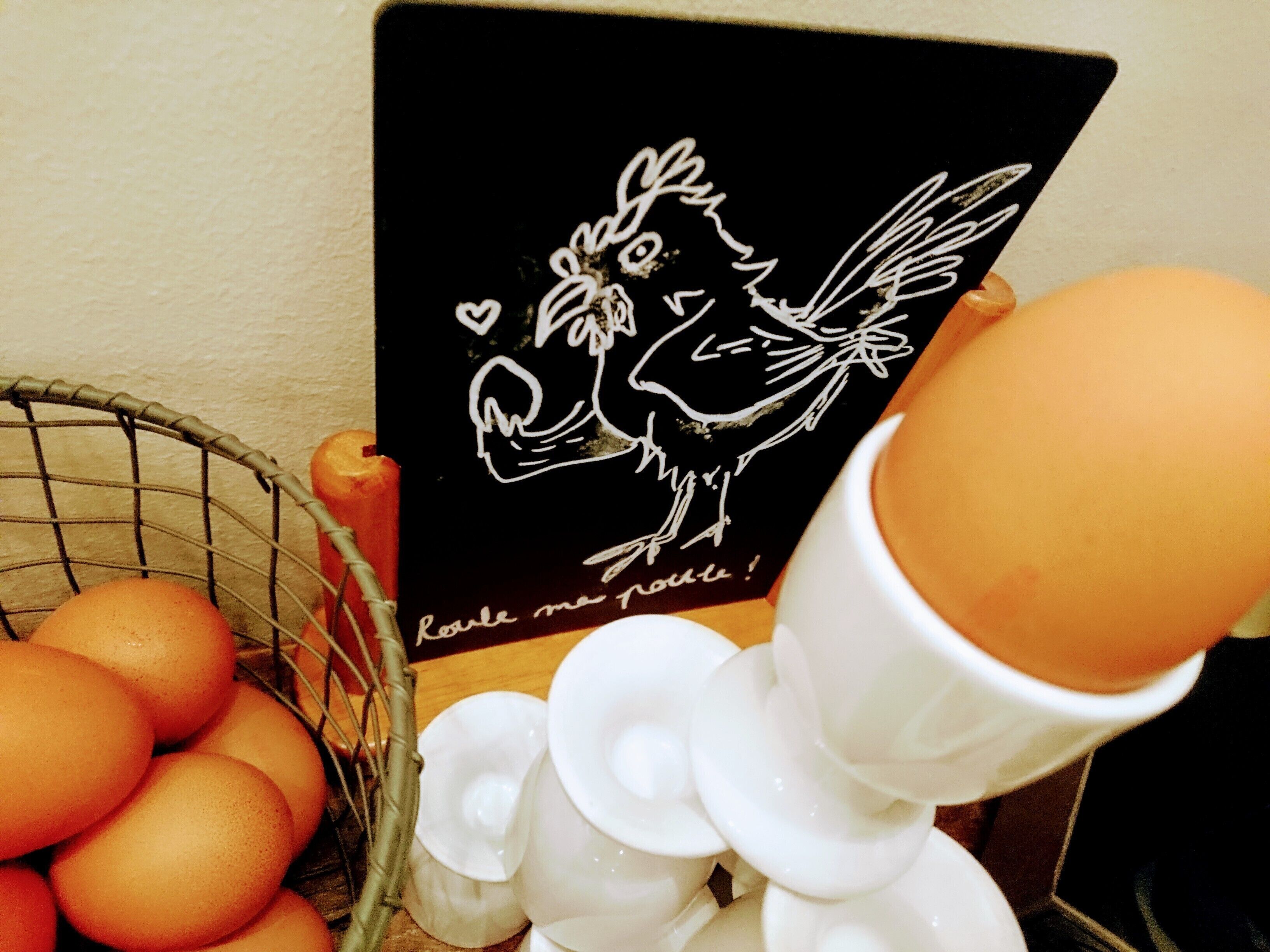 Una cesta de huevos, una tarjeta negra con un dibujo y texto, y un objeto de cerámica blanca.