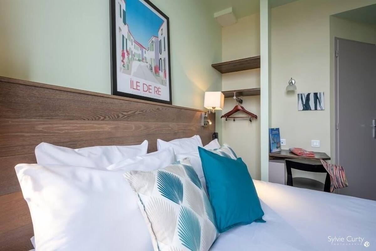 A hotel room with a wooden headboard, white bedding, and a framed picture of a street scene.