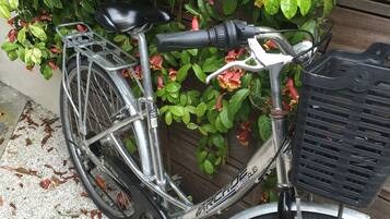 A bicycle parked on a gravel surface with a basket attached to the front and a seat.