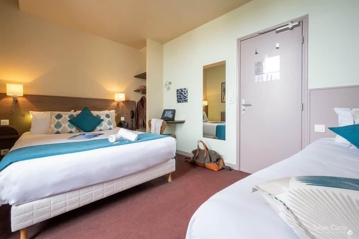 A hotel room with two beds, a wardrobe, a mirror, and a desk with a chair.