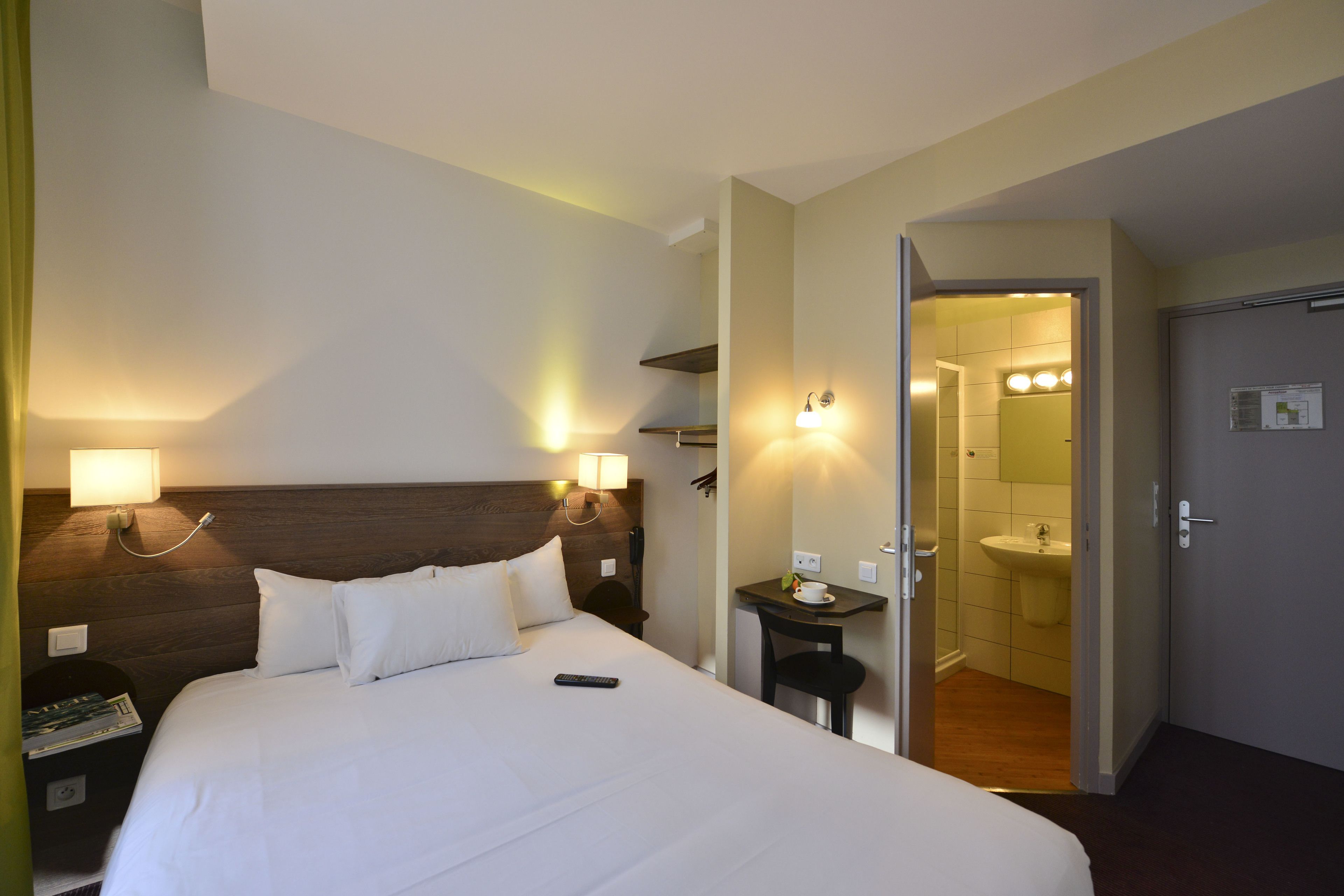 Ein Hotelzimmer mit Bett, Nachttisch, Lampe und Blick ins Badezimmer.
