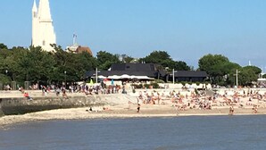 A coastal town with a prominent white church tower, a sandy beach, and a crowd of people. - Accostage Hotel (La Rochelle)