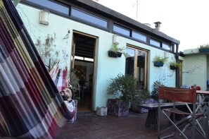 Edifici amb un gran portal obert, plantes en testos i una cadira a l'exterior.