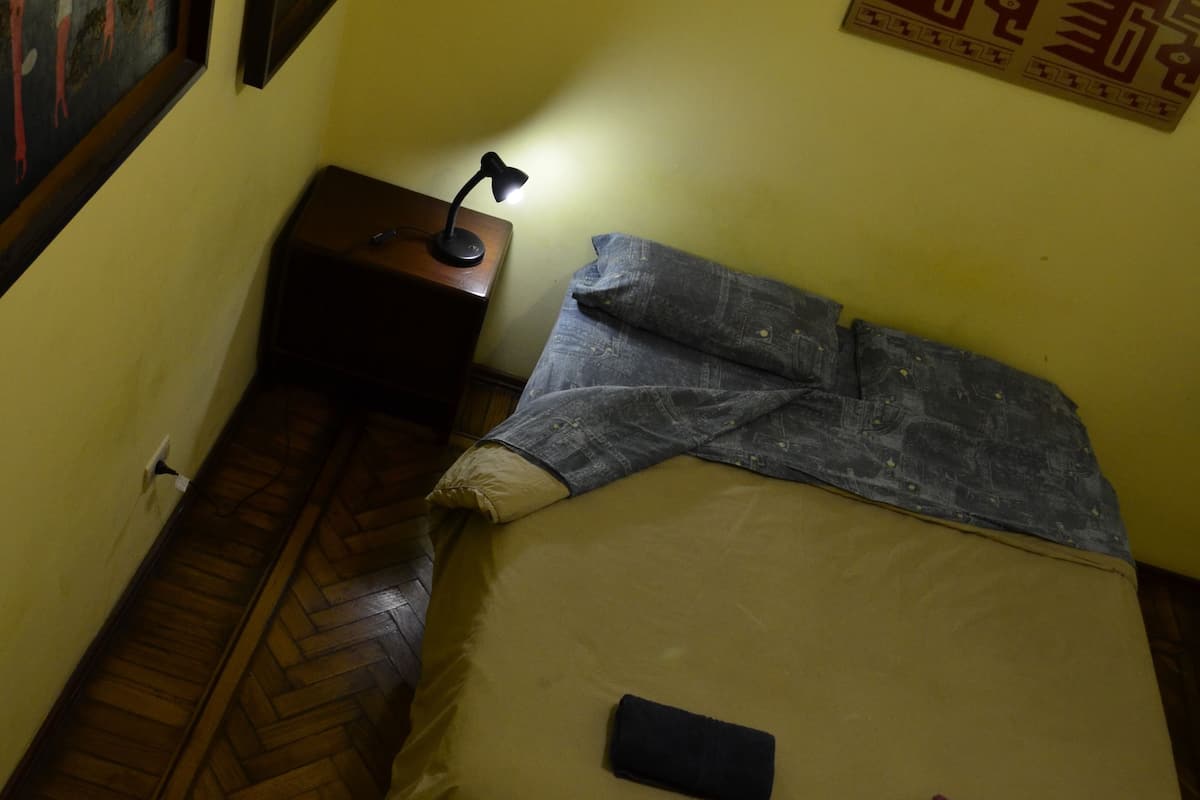 A room with a bed, a nightstand, a lamp, and a wall with framed artwork.