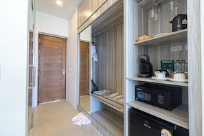 A modern hotel room with a wooden door, a walk-in closet with shelves, a microwave, and a coffee maker. - Three Trees Samui Resort - Sarocha Villa (Koh Samui)