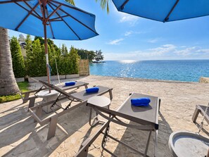 An outdoor seating area with tables and chairs, a large umbrella, and a view of the sea. - Three Trees Samui Resort - Sarocha Villa (Koh Samui)
