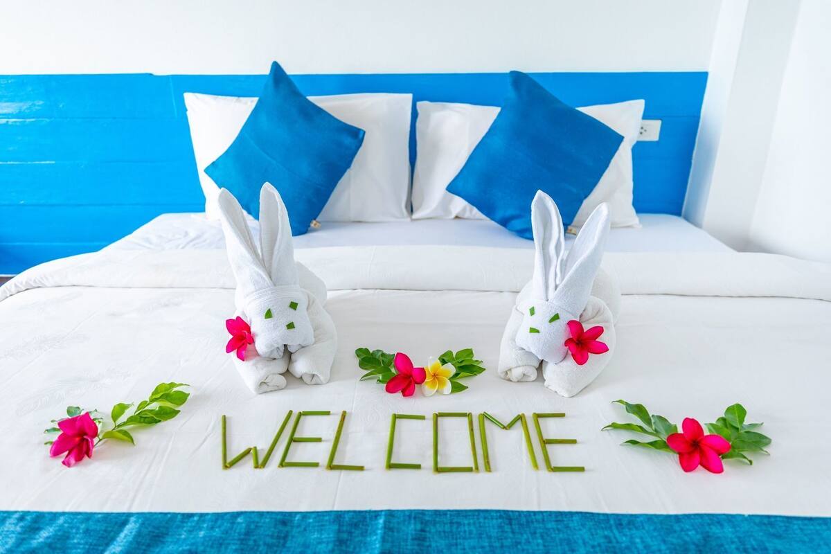 Uma cama com roupa de cama branca, duas toalhas brancas em formato de coelhos e a palavra 'WELCOME' escrita com folhas verdes.