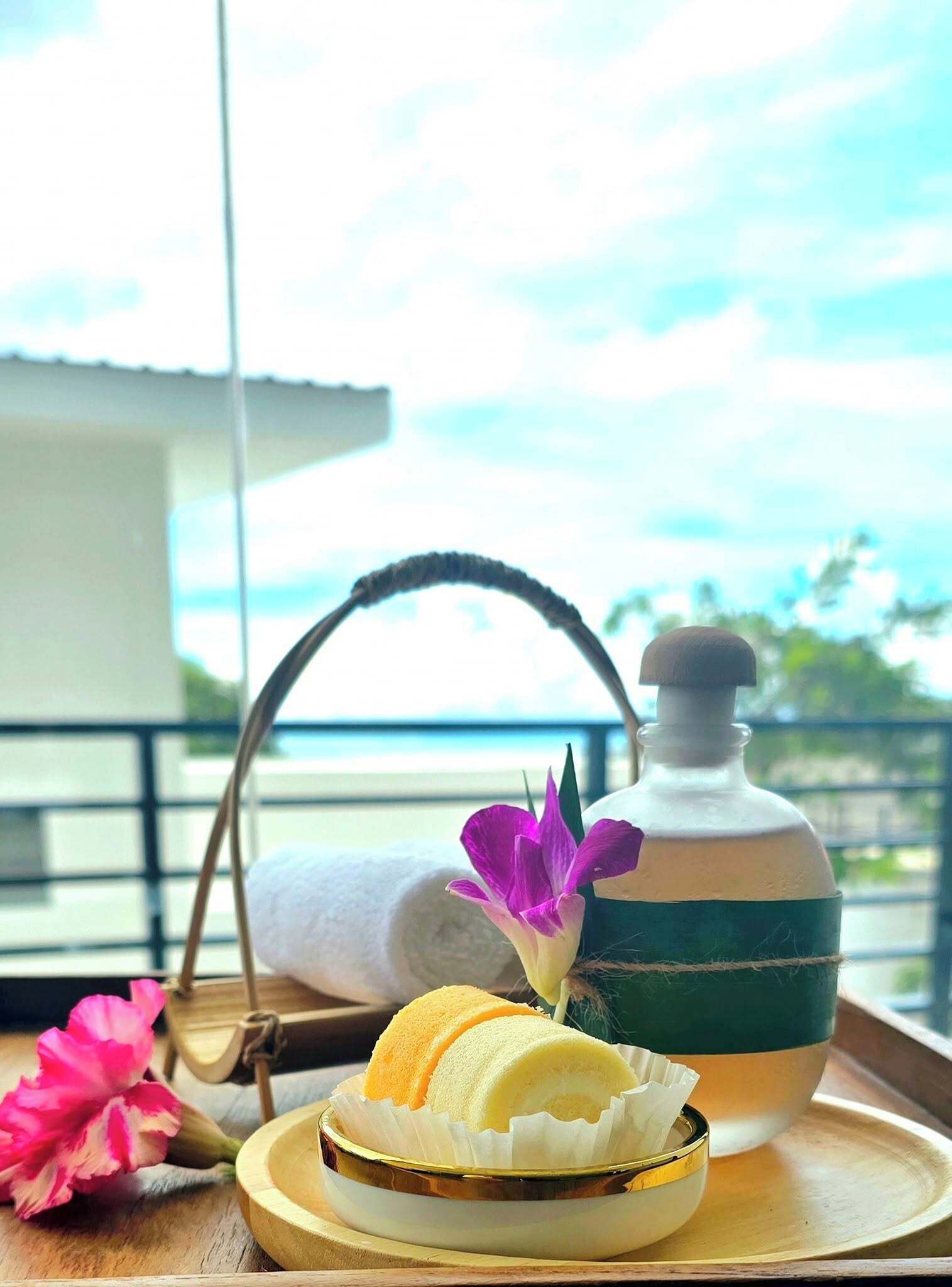 A tray with a bottle, a rolled towel, and a bowl with a flower and a rolled item.