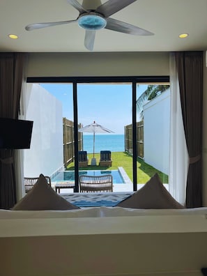 Quarto com uma grande janela com vista para uma piscina e para o mar.