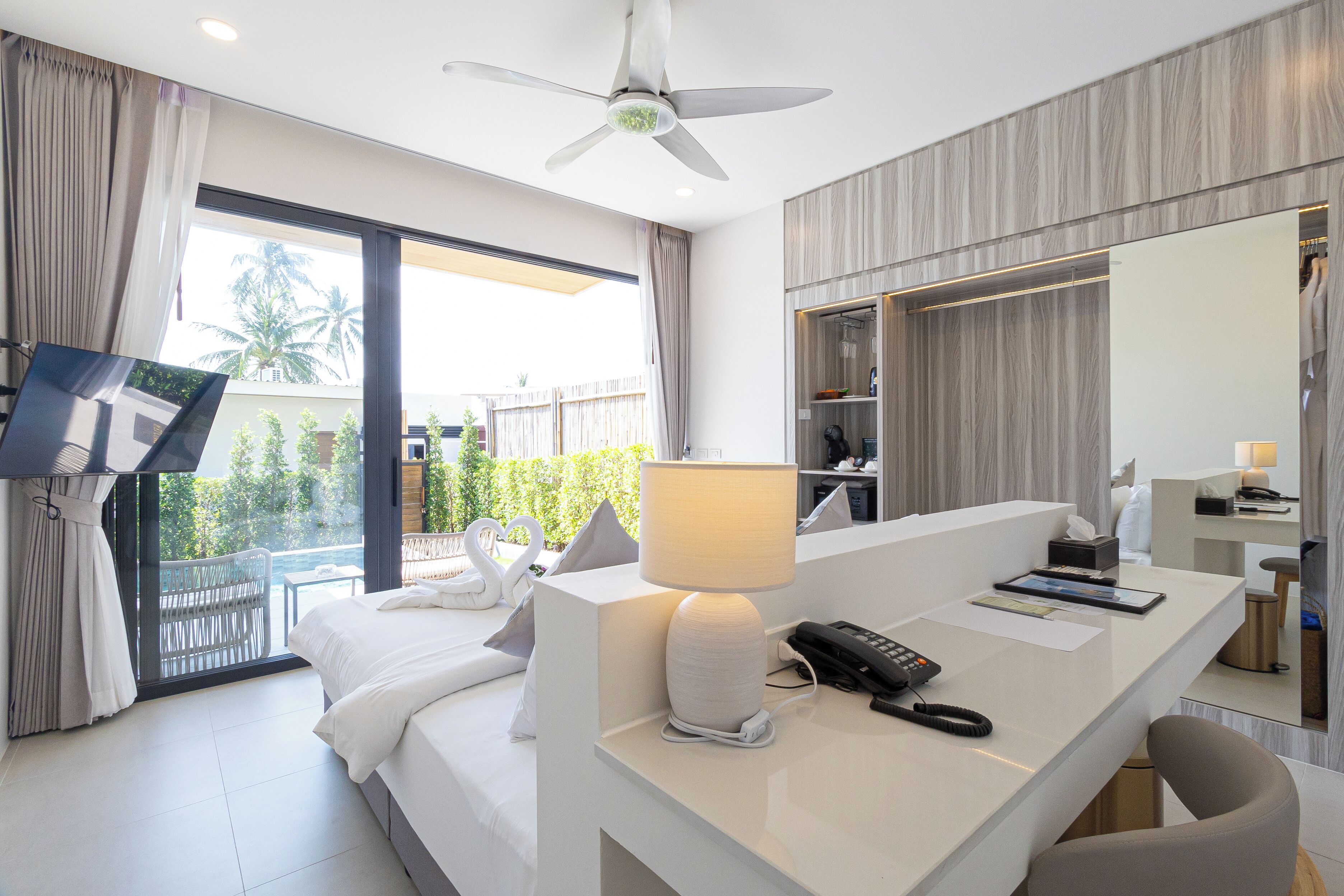 A modern hotel room with a bed, a desk with a lamp, a phone, and a large mirror.