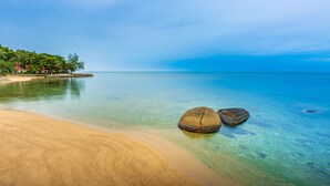 A beach with clear water, two large rocks, and a distant shoreline with buildings. - Three Trees Samui Resort - Sarocha Villa (Koh Samui)