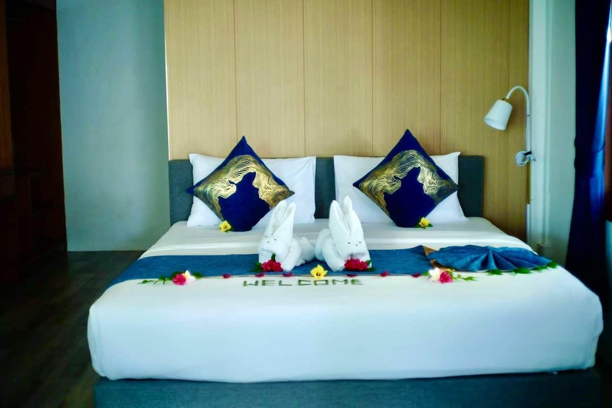 Cama bem arrumada com um letreiro 'WELCOME', duas almofadas decorativas e uma luminária na parede.