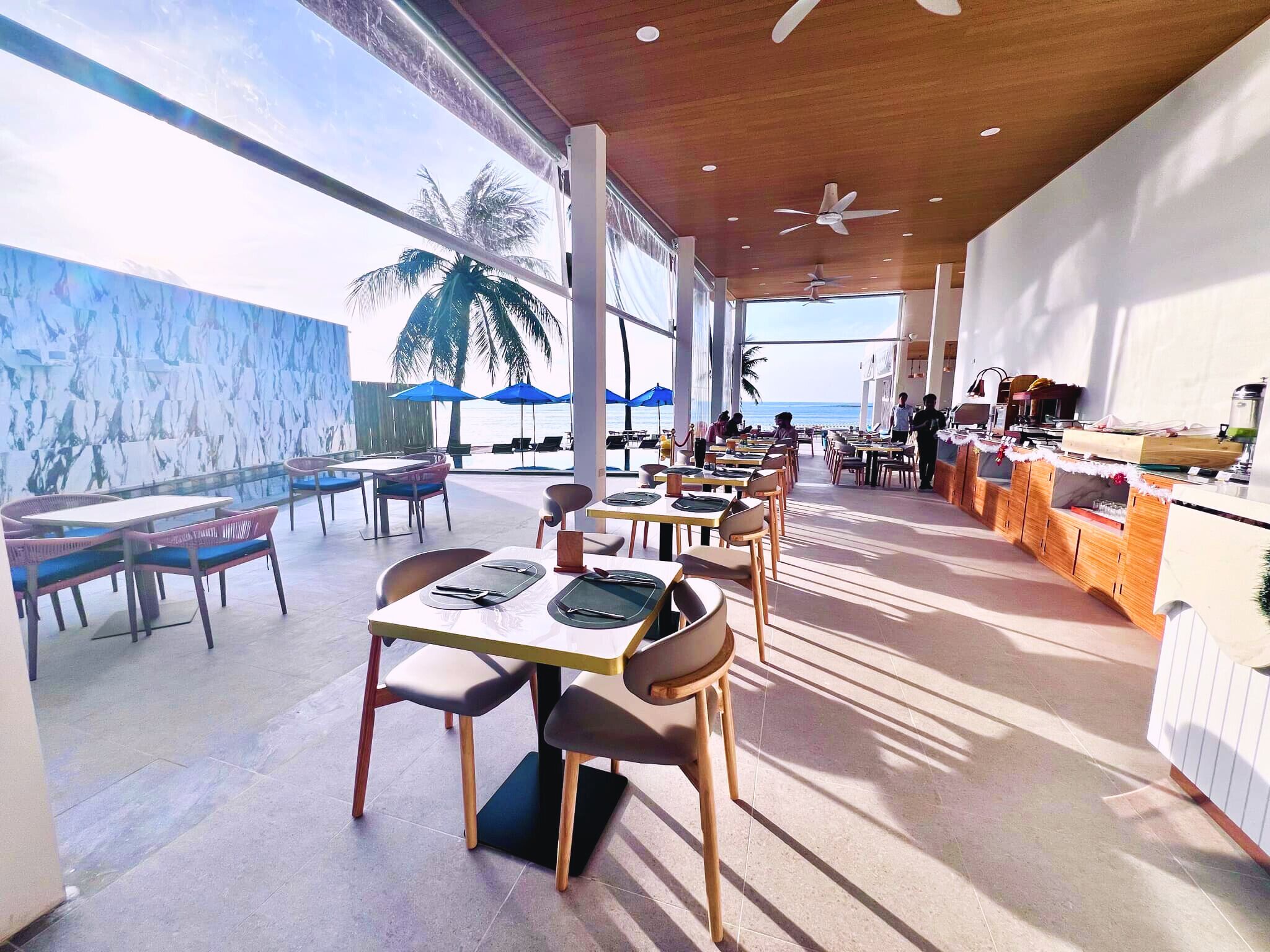 A spacious outdoor dining area with tables and chairs, a view of the beach, and a bar area.