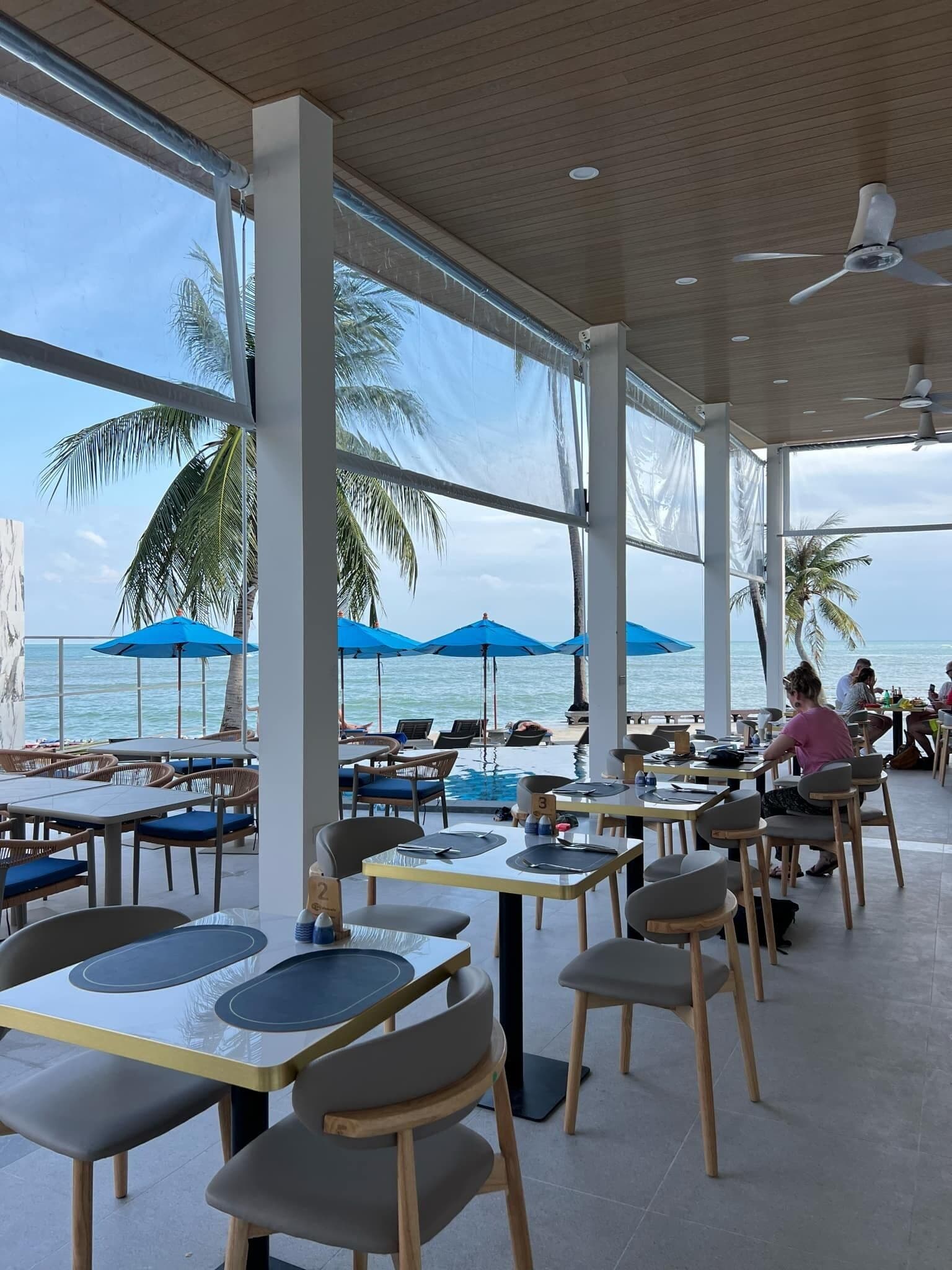 An outdoor dining area with tables and chairs, large windows, and blue umbrellas.