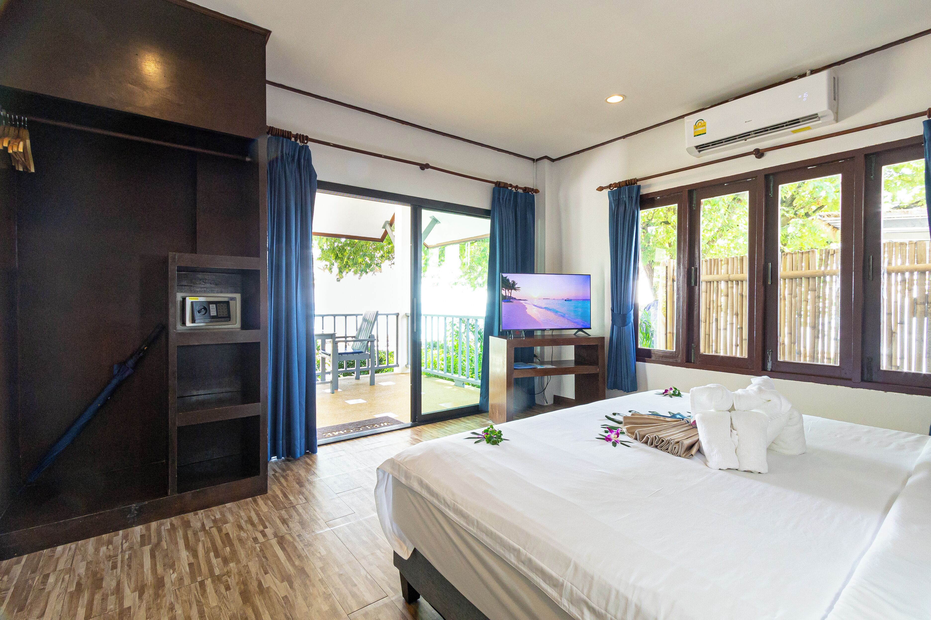 Habitación de hotel con cama, televisión, armario y balcón con vistas a zonas verdes.
