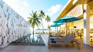 A pool area with lounge chairs and umbrellas, palm trees, and a view of the ocean. - Three Trees Samui Resort - Sarocha Villa (Koh Samui)