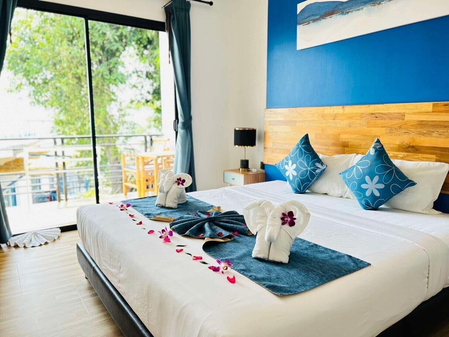 Quarto de hotel com uma cama grande, cabeceira de madeira, vista para o verde lá fora e um quadro na parede.