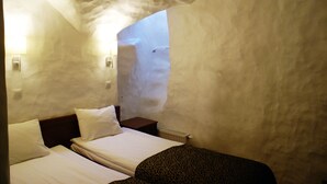 Quarto com duas camas, cabeceira de madeira, mesa de cabeceira e luminária fixada na parede.