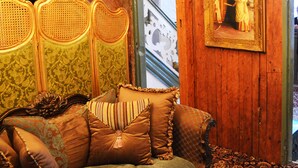 Um interior em madeira com um sofá, almofadas estampadas, um candelabro e um quadro na parede.