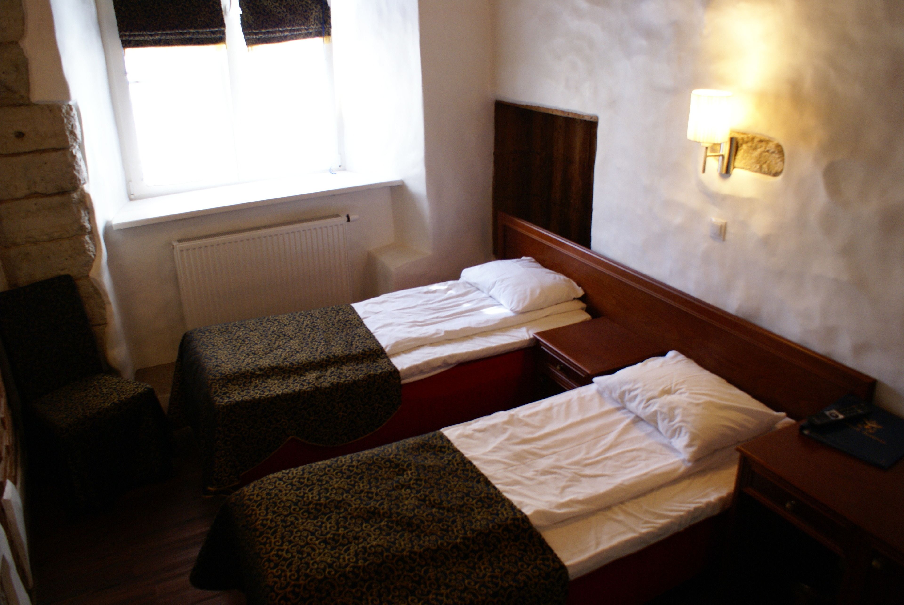 Una habitación pequeña y poco iluminada, con dos camas individuales, un muro de piedra y una ventana con cortinas.