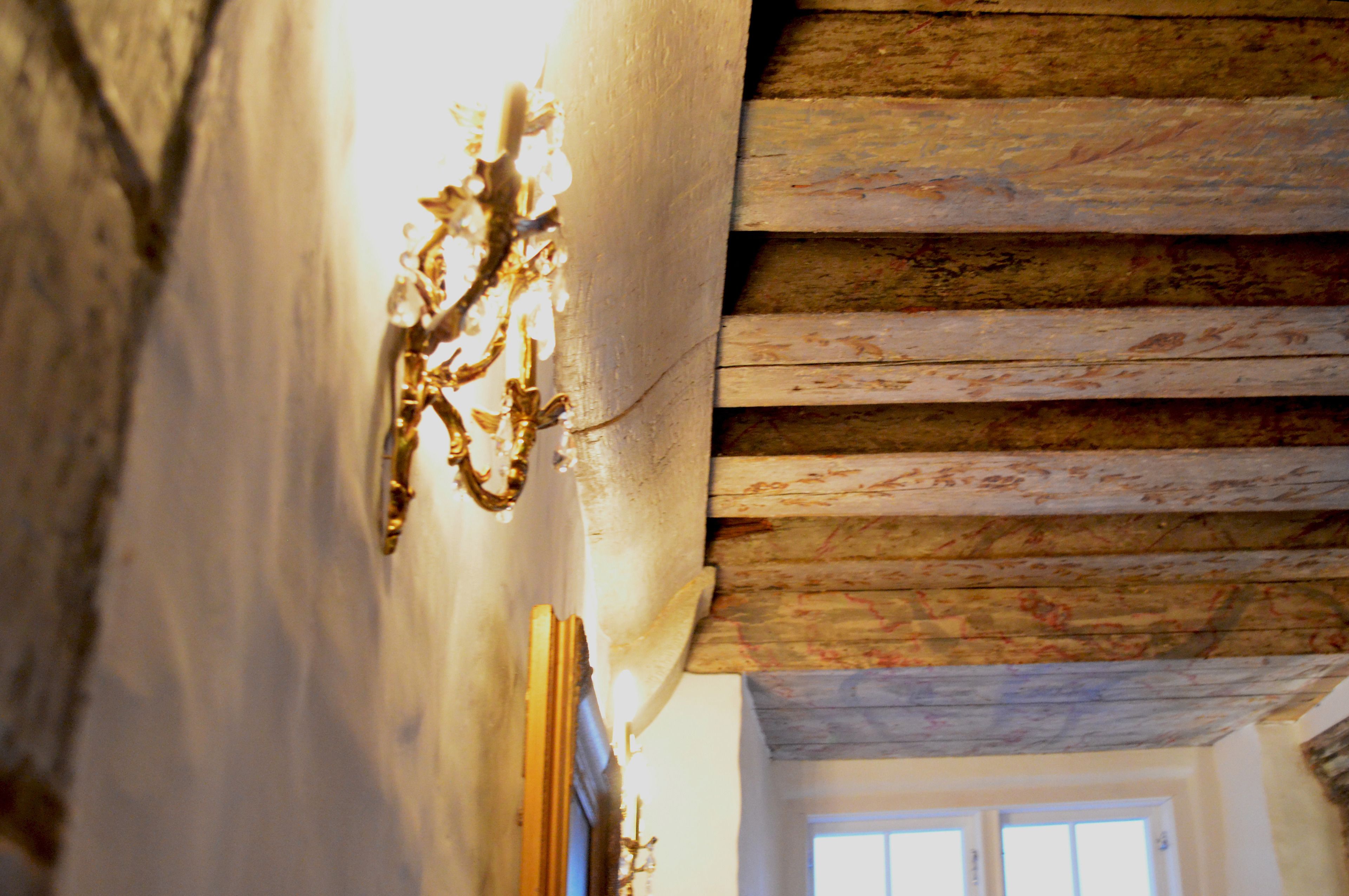 Un intérieur rustique avec des poutres apparentes et un luminaire décoratif fixé au mur.