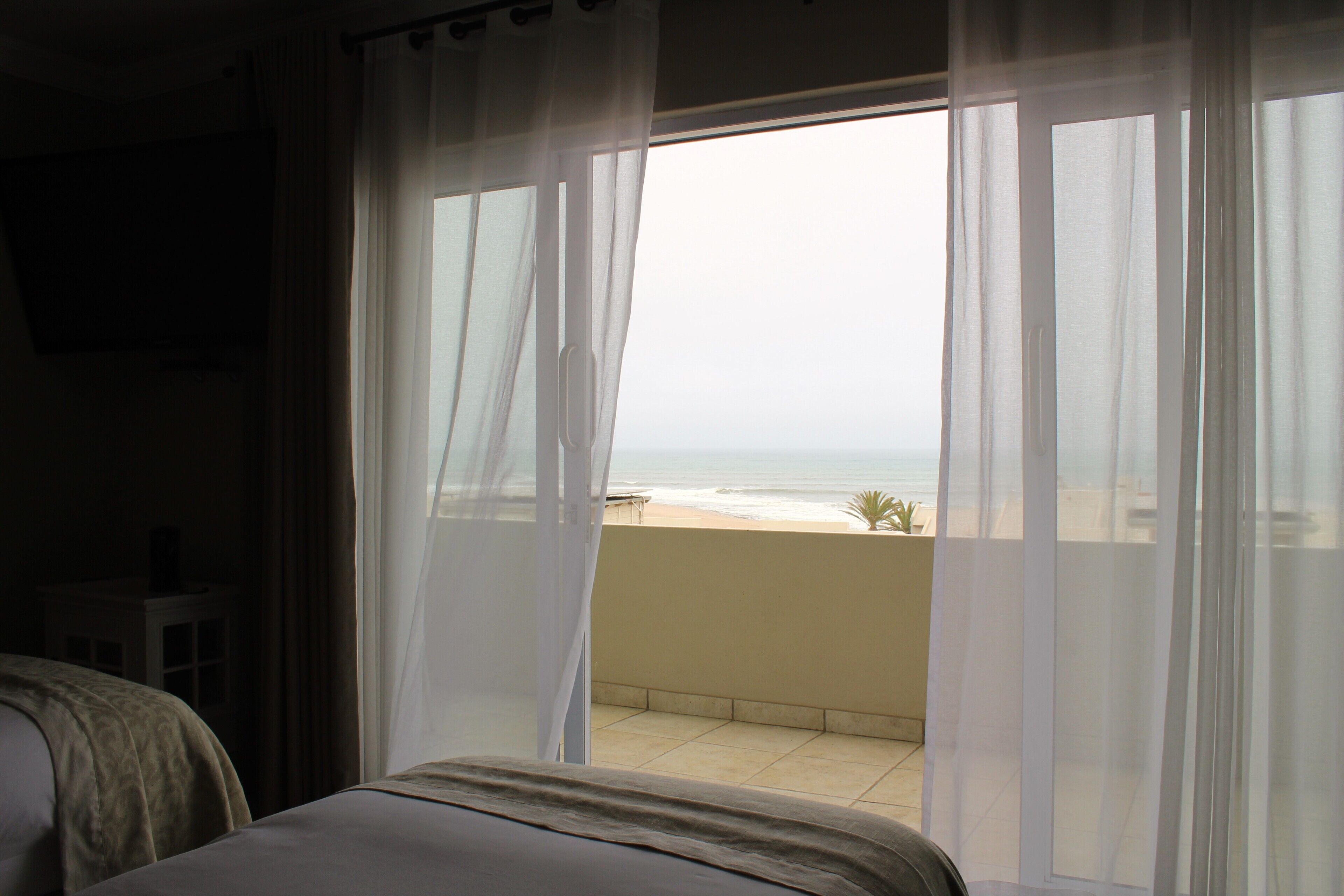 Una habitación con cama y vista a la playa a través de cortinas traslúcidas.