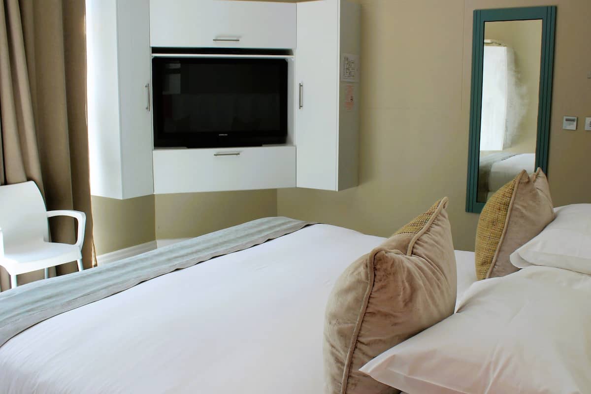 A hotel room with a bed, a chair, a television mounted on the wall, and a mirror.