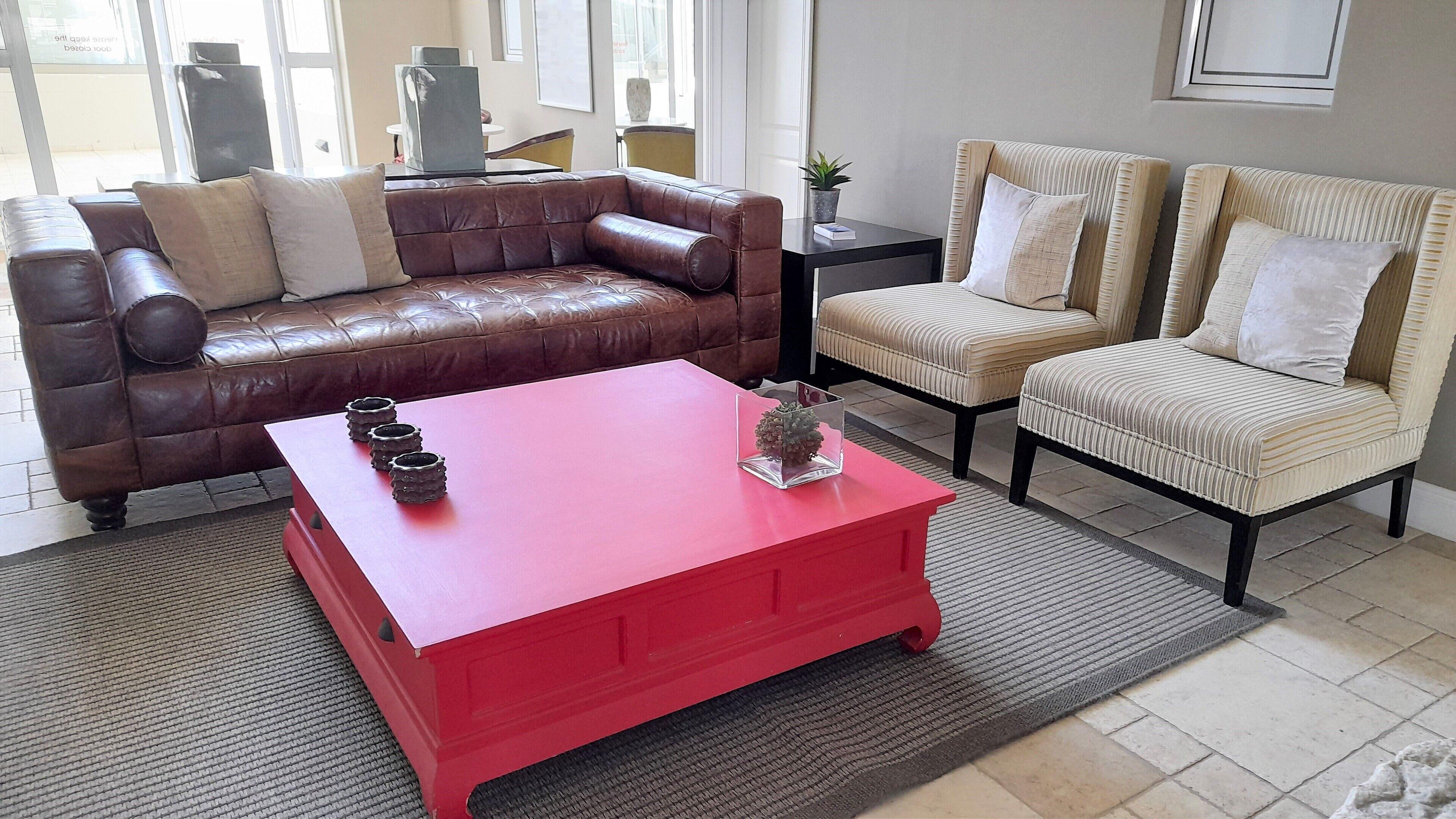 A living room with a brown leather sofa, a beige armchair, and a red coffee table.