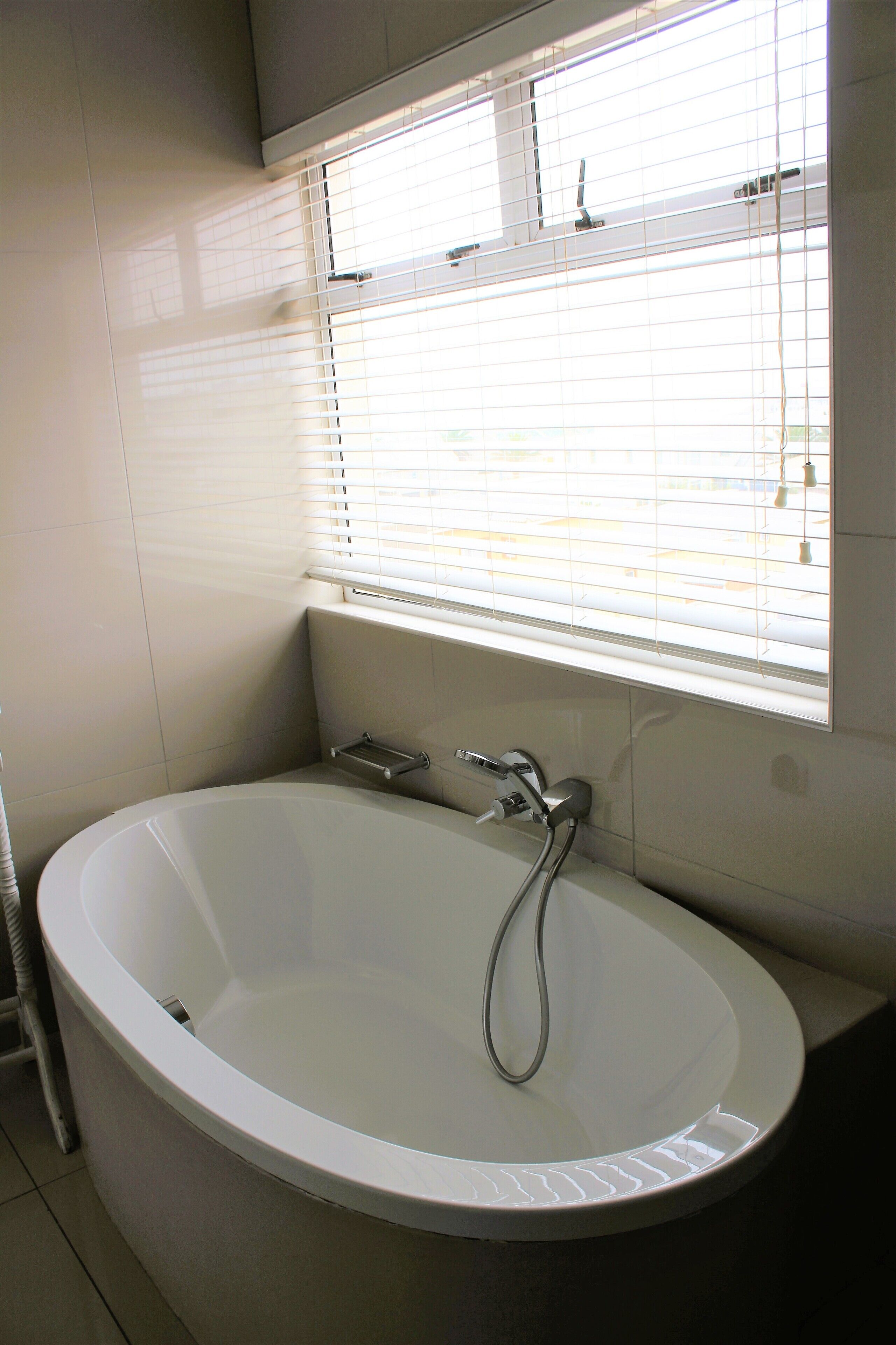 Ein modernes Badezimmer mit einer freistehenden Badewanne, einem Fenster mit Jalousien und einem Handtuchhalter.