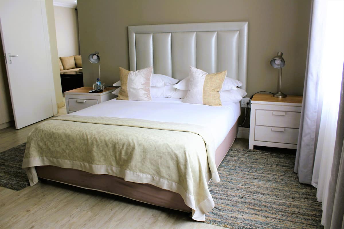 A neatly made bed with a white headboard and multiple pillows, a bedside table with a lamp, and a carpeted floor.