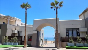 A modern building with a central archway, palm trees, and a view of the sea. - Atlantic Villa Boutique Guesthouse (Swakopmund)