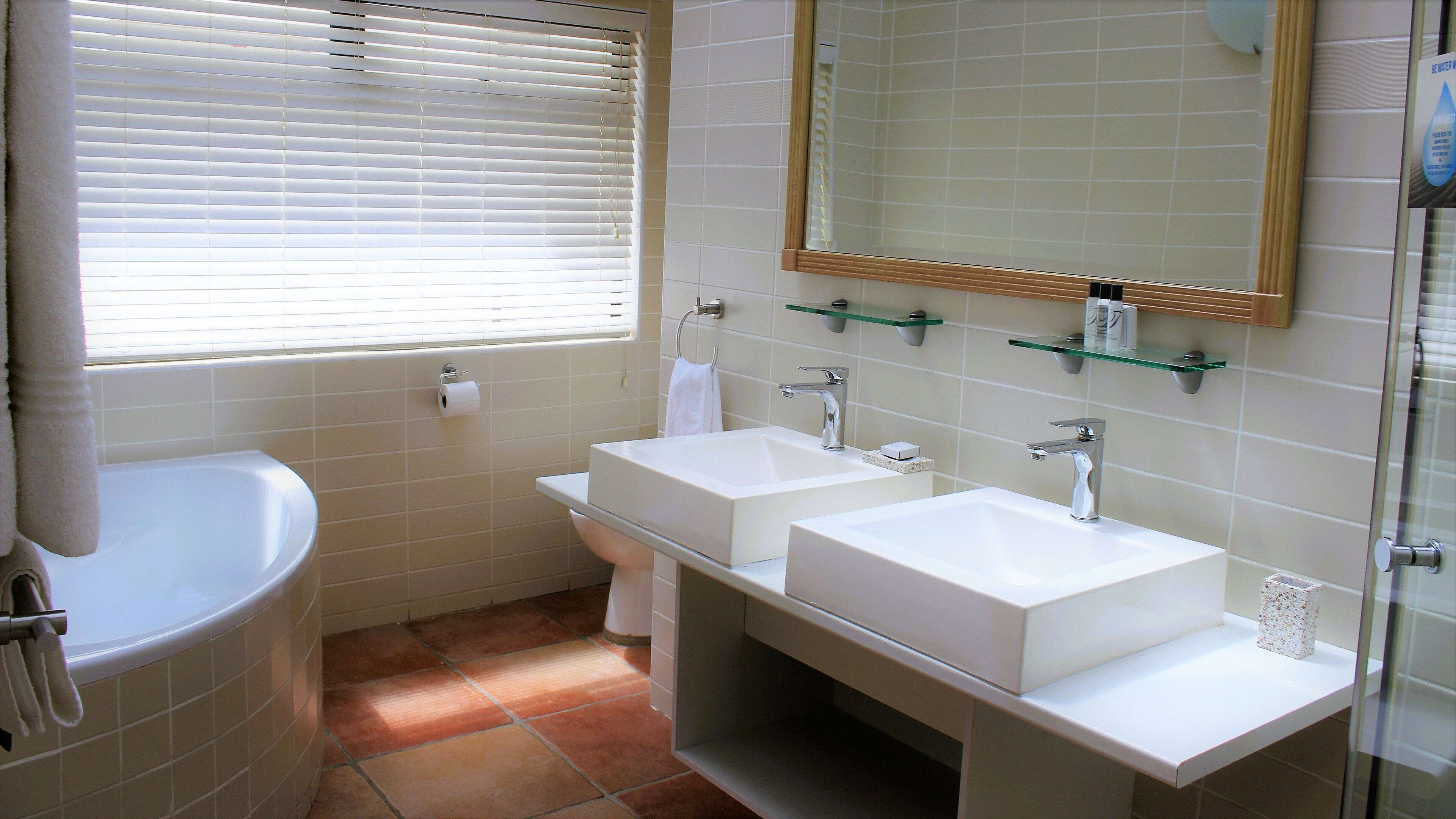 Ein Badezimmer mit einer Badewanne, zwei Waschbecken, einem Spiegel und einem Fenster mit Jalousien.