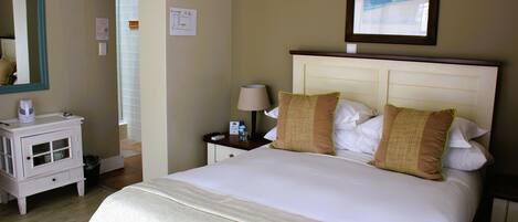 A hotel room with a bed, a nightstand with a lamp, a small table with a kettle, and a mirror on the wall.