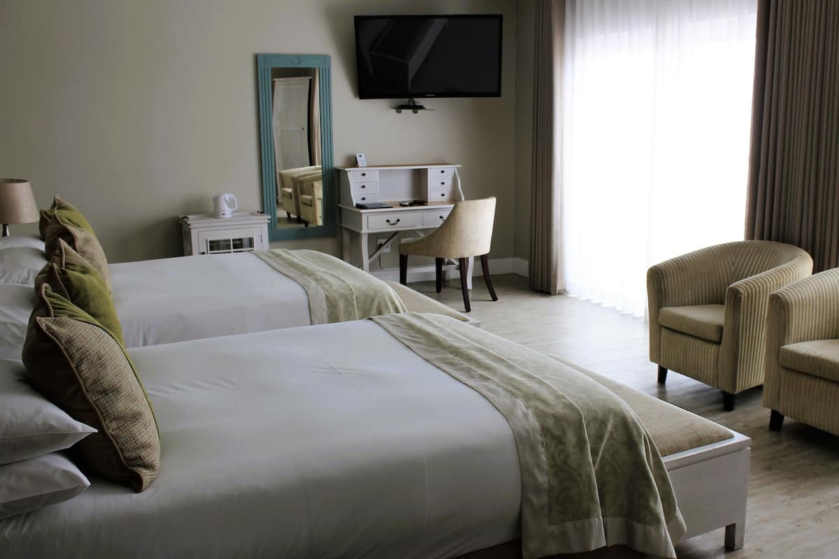 A hotel room with two beds, a desk, a chair, and a TV.