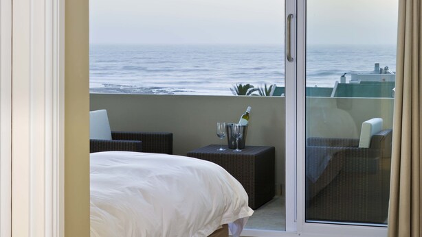 A balcony with a bed, a wicker chair, a small table with a bottle and glasses, and a view of the ocean. - Atlantic Villa Boutique Guesthouse (Swakopmund)