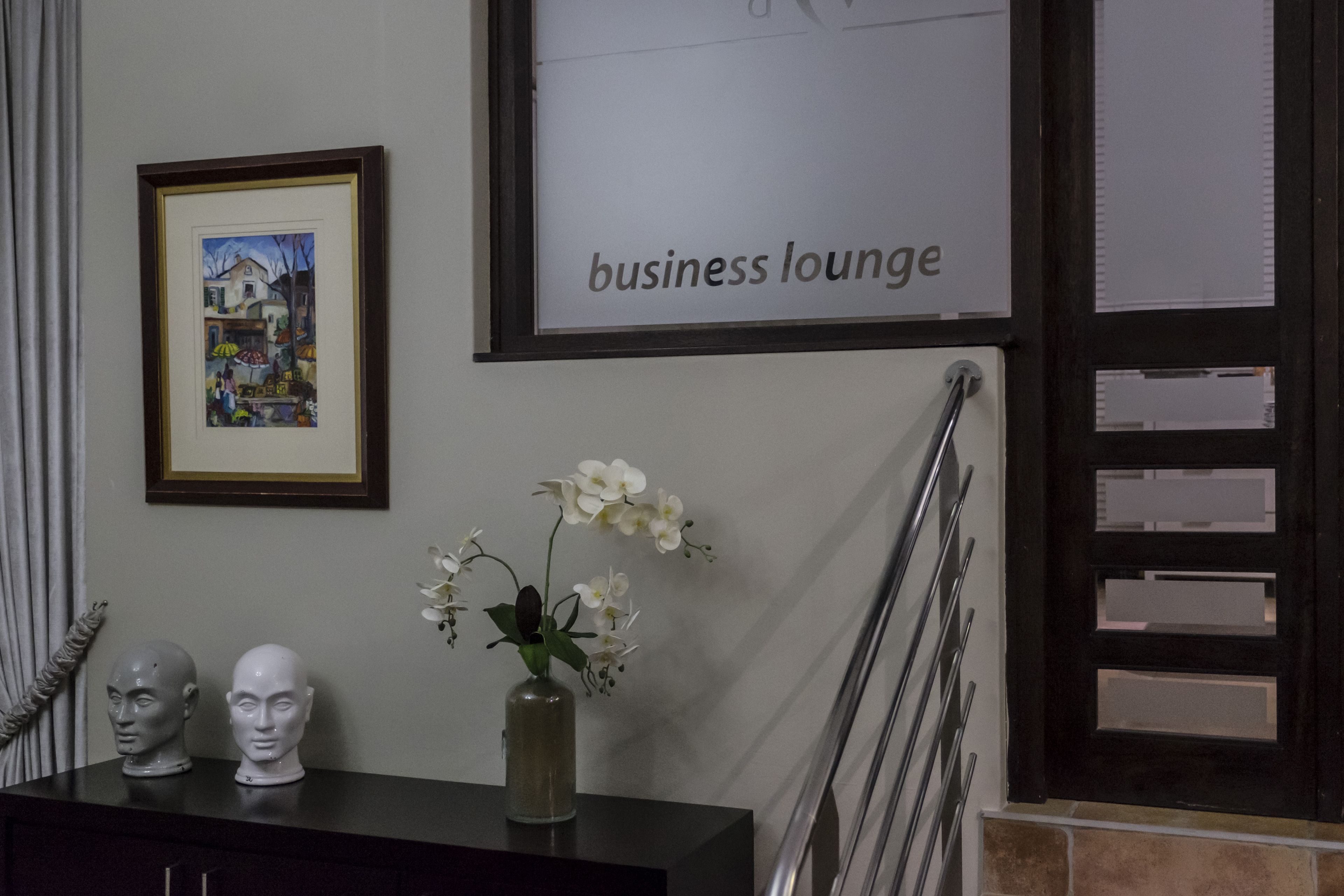 A business lounge with a framed painting, a vase with white flowers, and two bust sculptures on a dark surface.