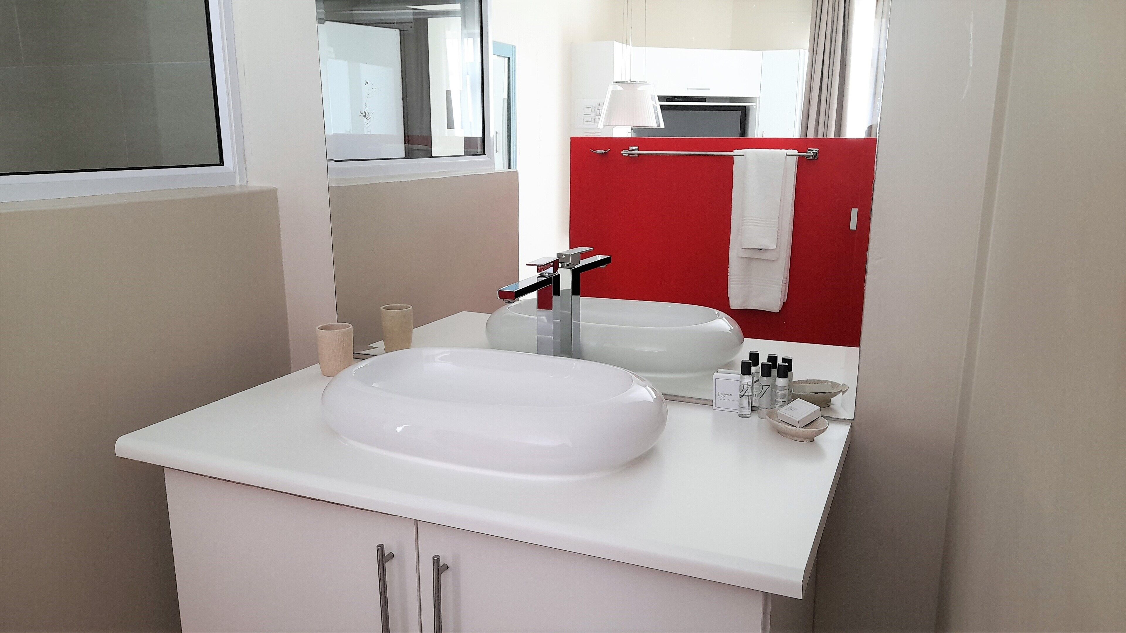 A modern bathroom with a white sink, a red accent wall, and a large mirror.