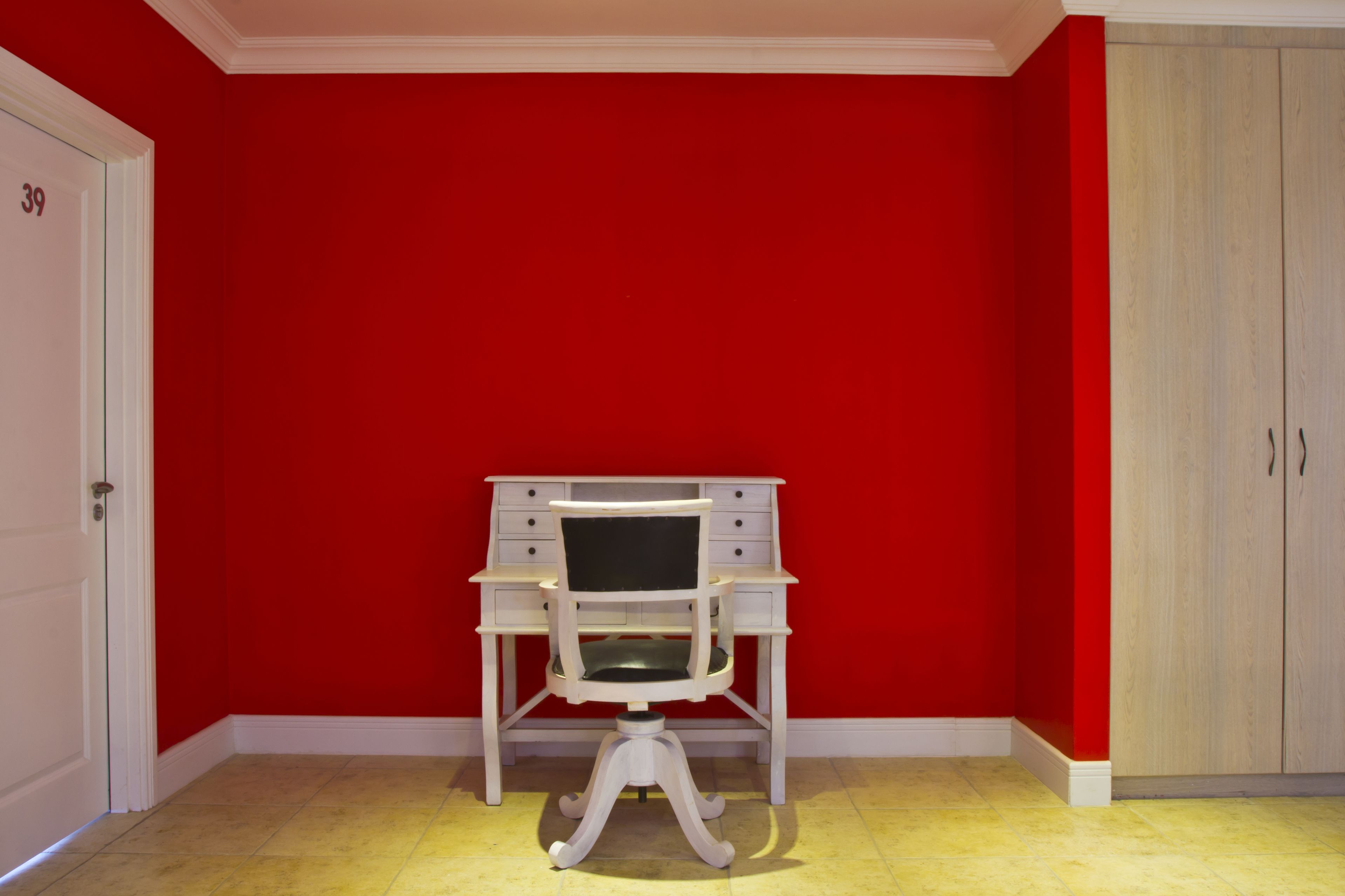 A room with a red wall, a white desk with drawers, and a white door with the number 39.