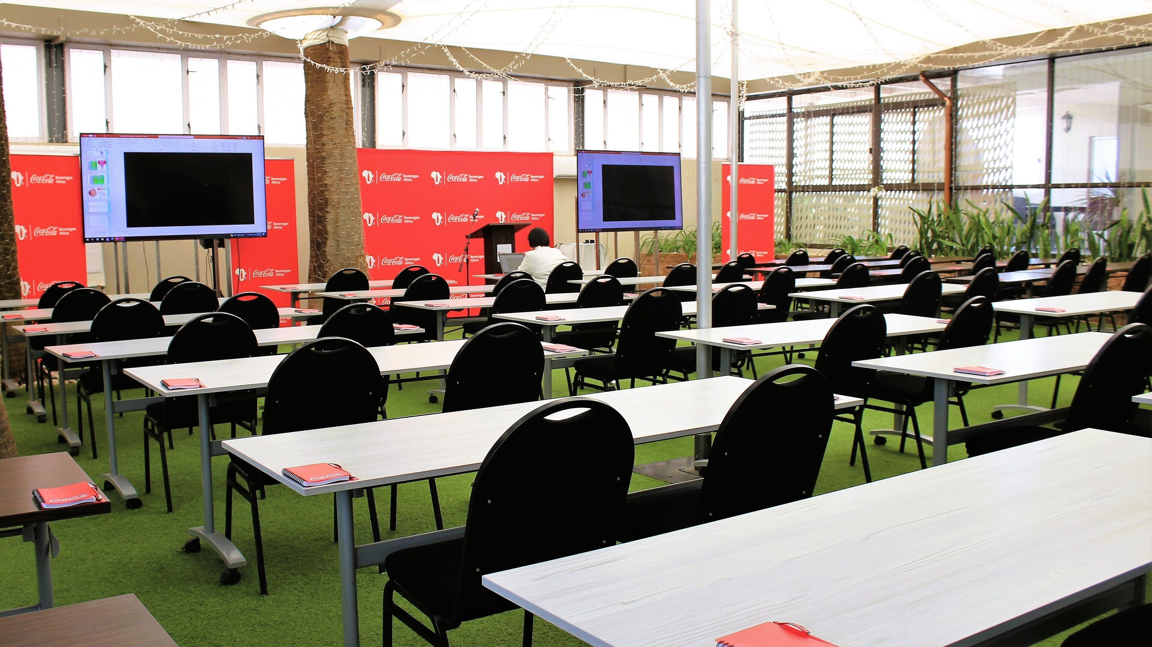 Une salle de conférence équipée de plusieurs tables et chaises, de grands écrans et de bannières à l’effigie de Coca-Cola.