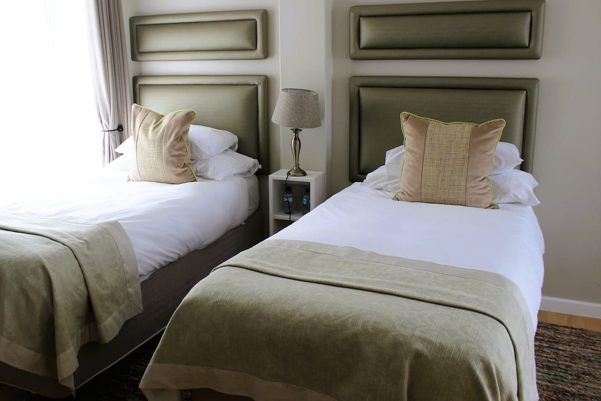 A hotel room with two beds, each with a headboard, a nightstand with a lamp, and a window with curtains.