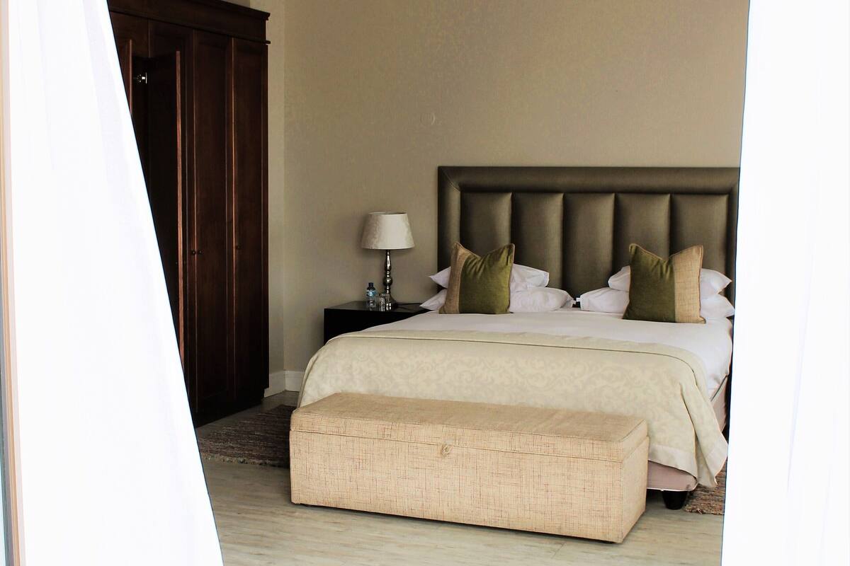 A bedroom with a large bed, a nightstand, a lamp, and a wooden wardrobe.