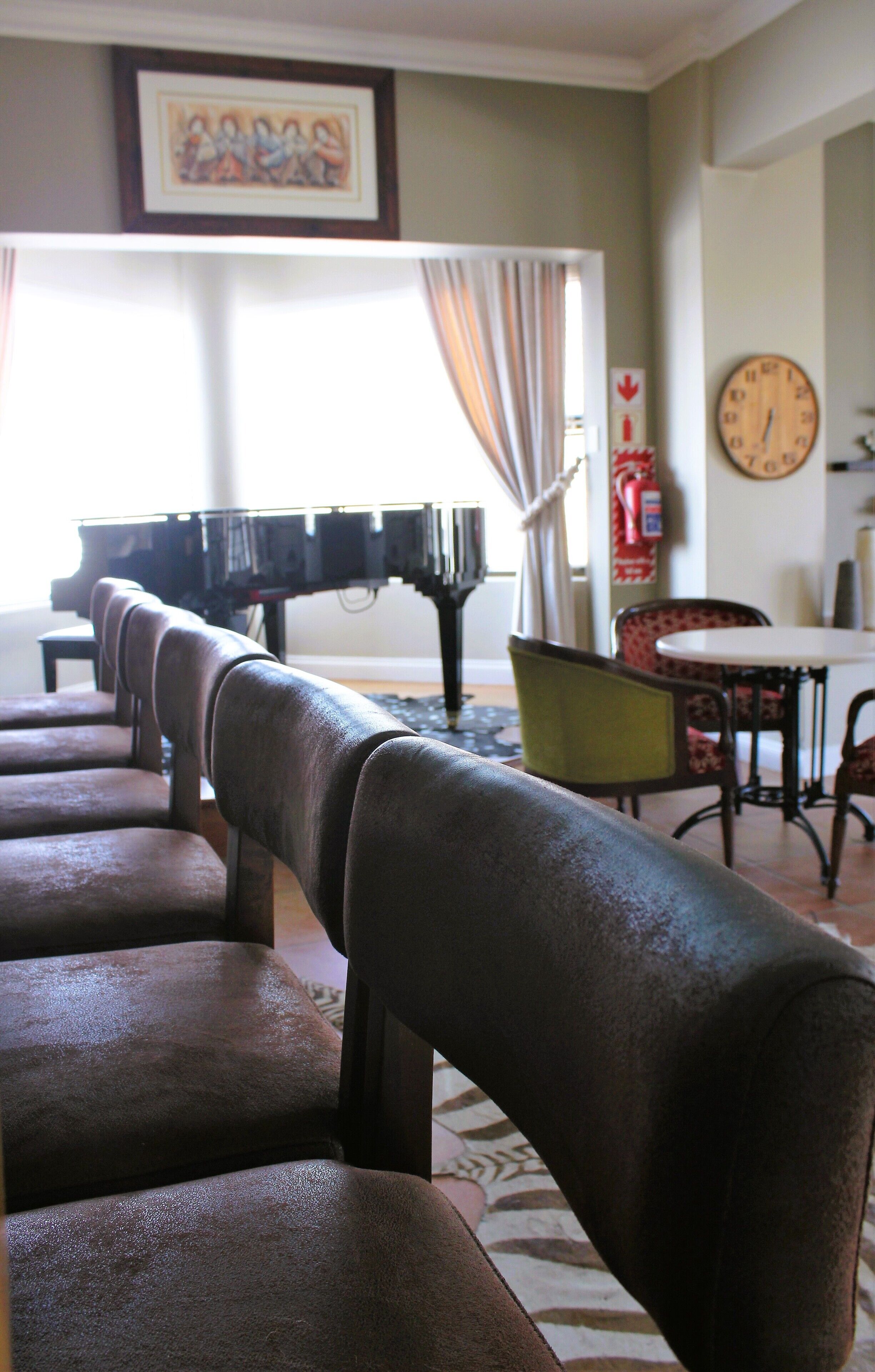 A piano in a room with a patterned rug, a clock on the wall, and a framed picture above the piano.